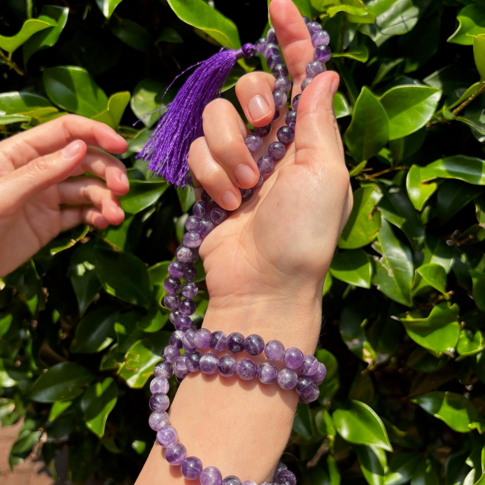 model with amethyst mala necklace wrapped around her hand on greenery background