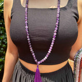 model wearing a black tank top in front of greenery with an amethyst mala around her neck