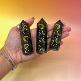 Three black crystal points with star and moon designs held in a hand against a gradient background.