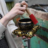 Person holding a singing bowl with a decorative cover, outdoors.