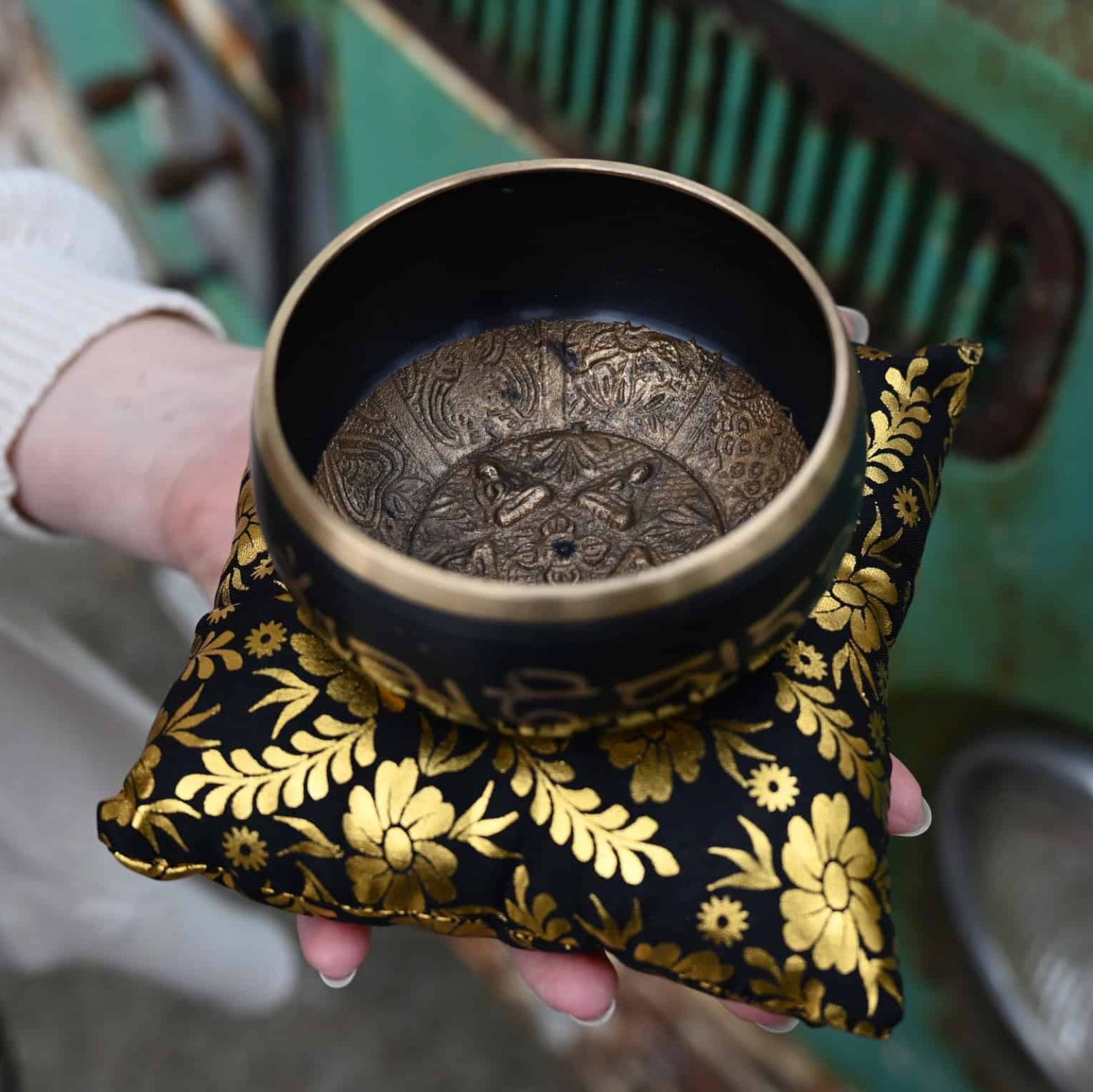 Person holding a black bowl with intricate design on a floral cushion