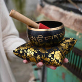 Person holding a singing bowl with floral design on a cushion