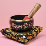 Tibetan singing bowl with wooden striker on a decorative pillow against a pink background