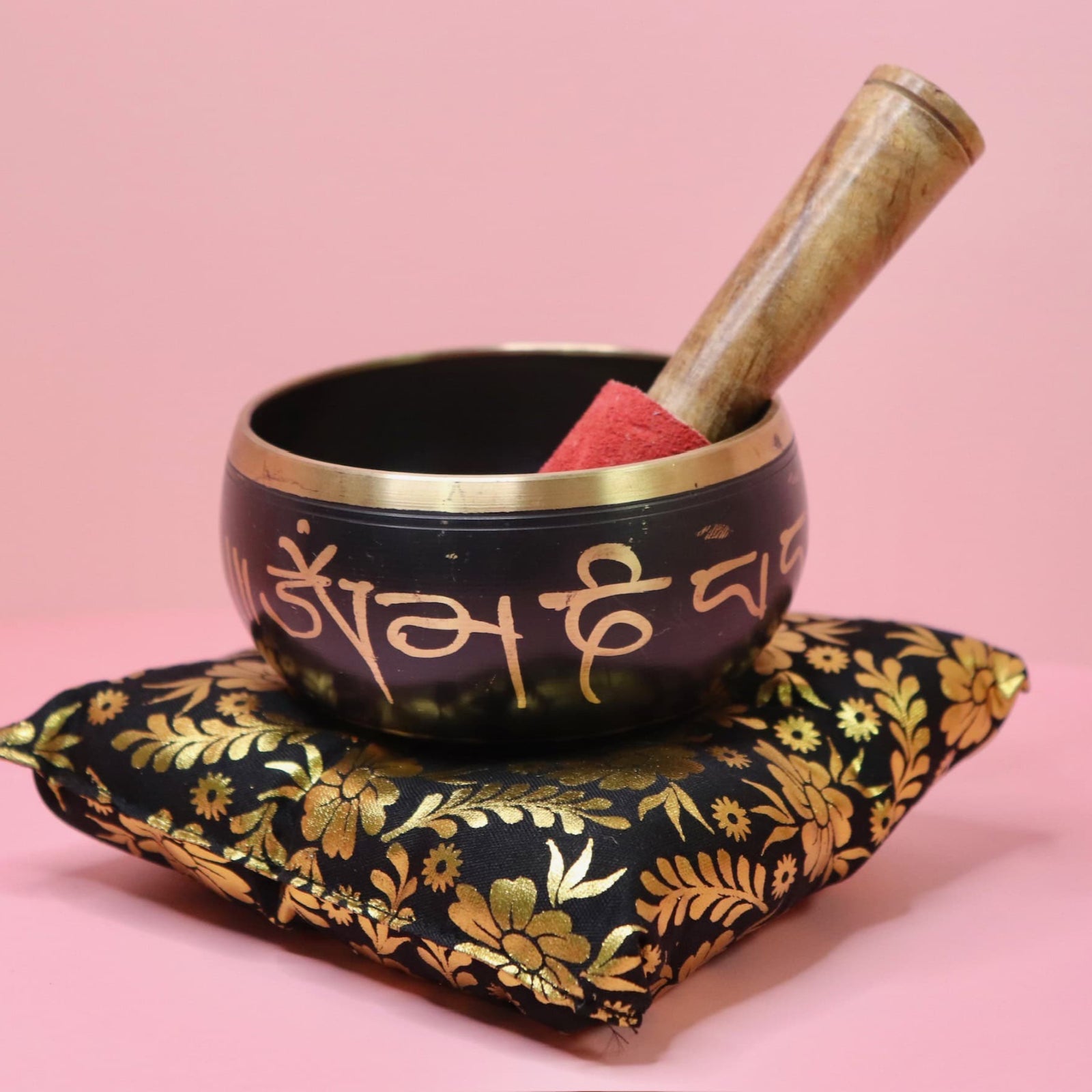 Tibetan singing bowl with wooden striker on a decorative pillow against a pink background