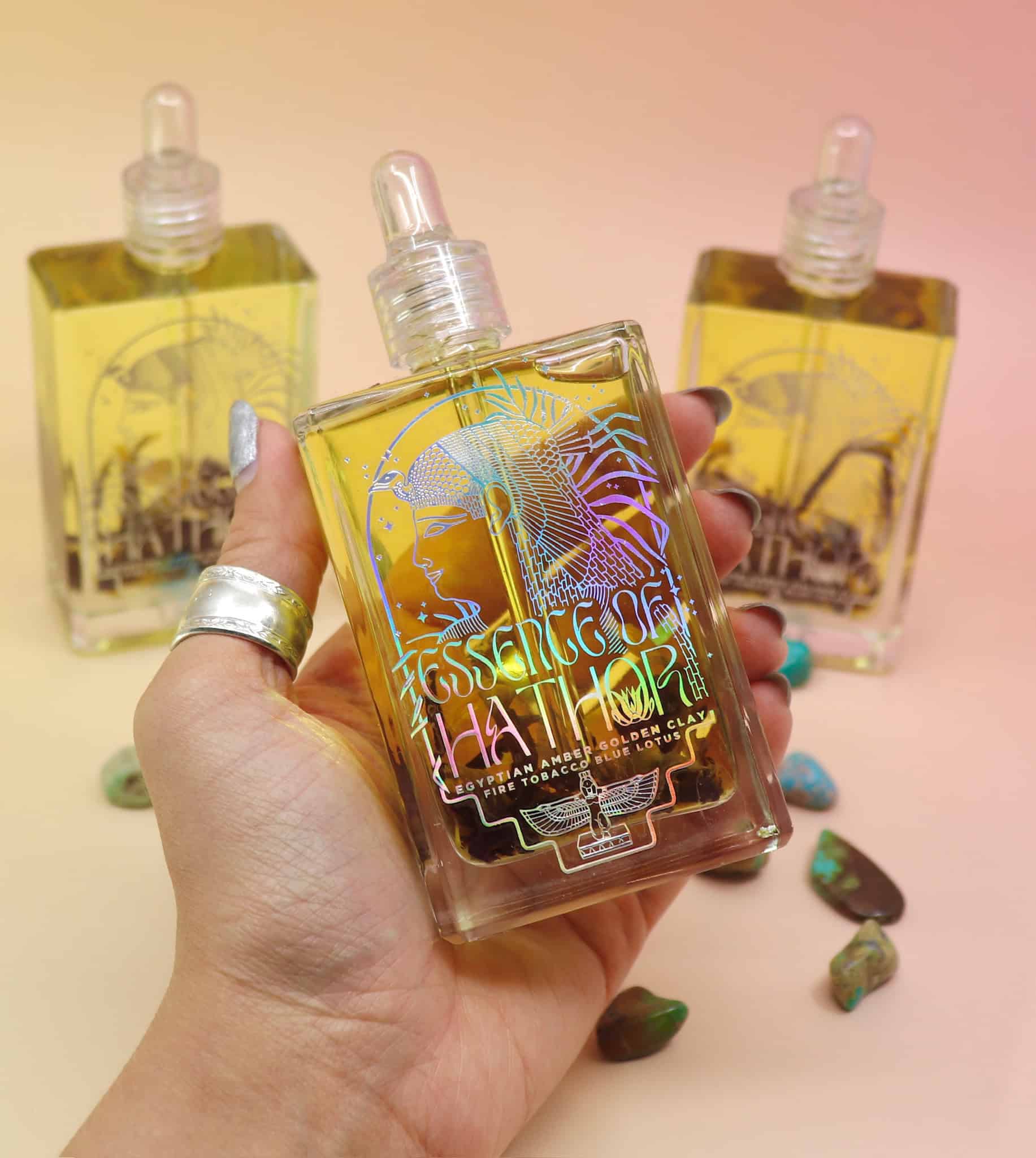 hand holiding a bottle of essence of hathor blue lotus oil with 2 bottles in the background