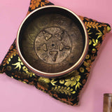 Decorative tibetan singing bowl on a floral pillow with a pink background