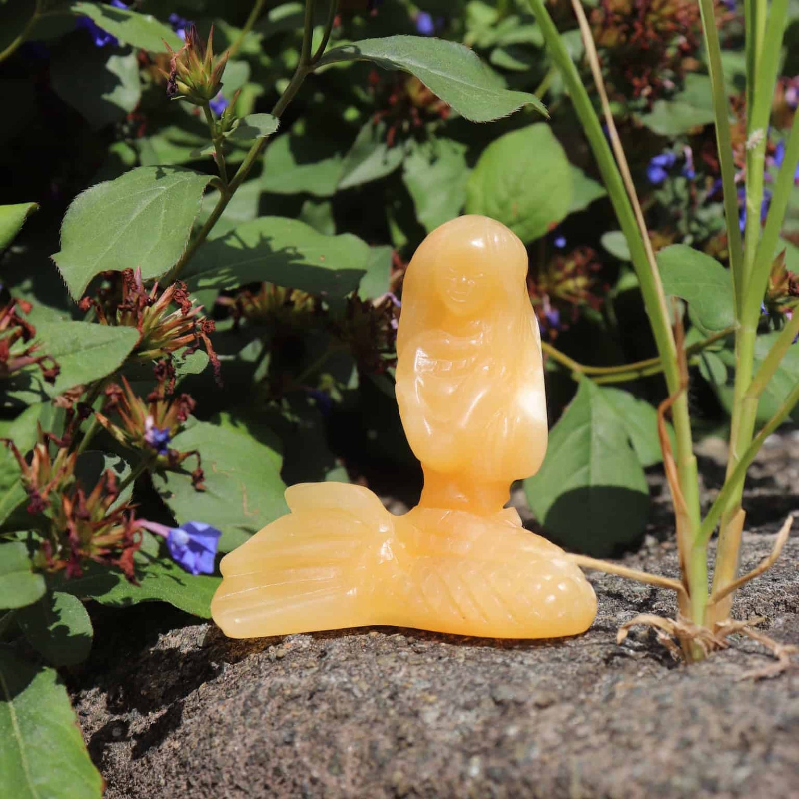 Orange plastic object resembling a stylized face on a stone surface with greenery in the background