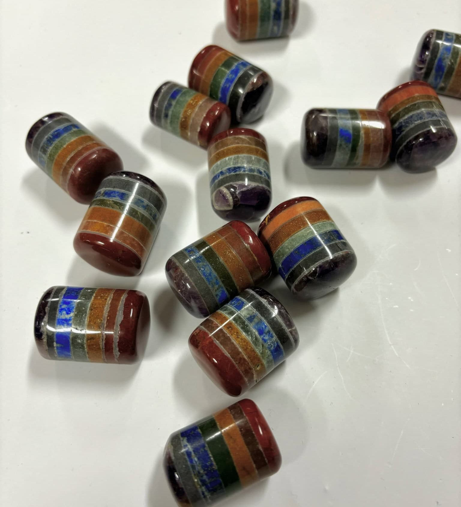 Multiple layered chakra cylinder tumbled stones on a white background, each featuring stacked colorful crystal layers