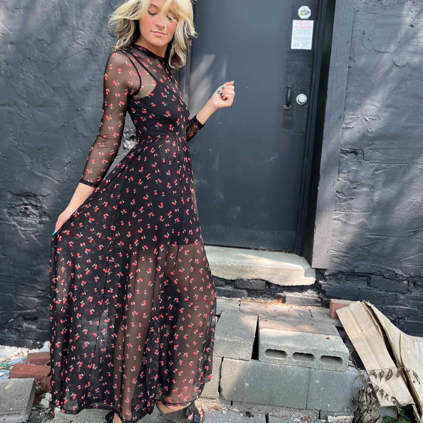 Woman in a black cherry mesh dress standing confidently on a stone step, looking down slightly.