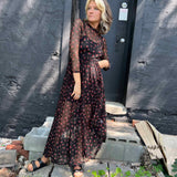 Woman swaying in a flowy cherry print maxi dress with sheer sleeves and mock neck.