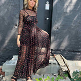 Woman holding out the hem of her cherry mesh maxi dress while standing on concrete steps.