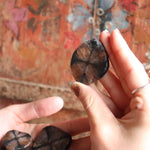Person holding a dark stone against a colorful, patterned fabric background