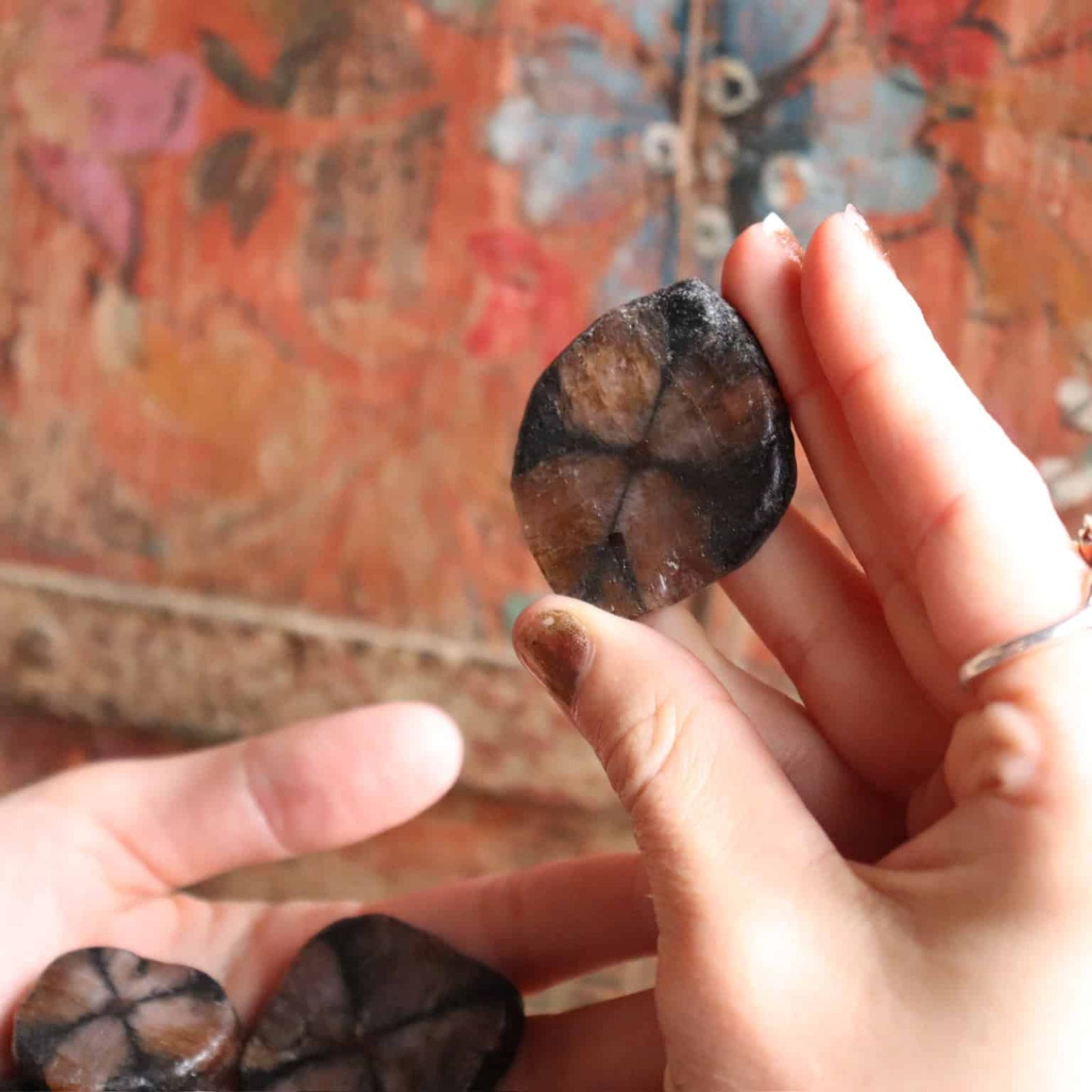 Person holding a dark stone against a colorful, patterned fabric background