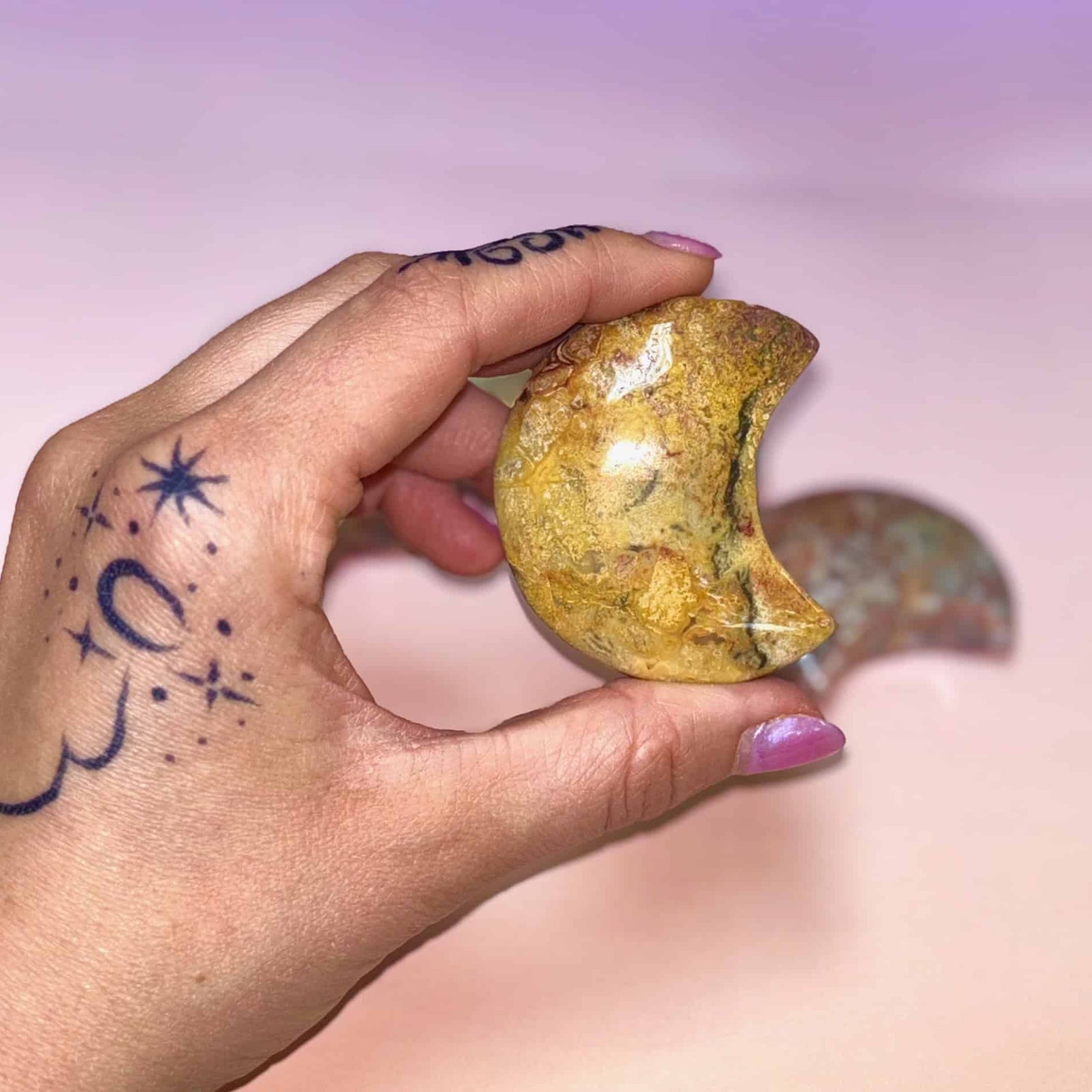 Hand holding a yellowish stone with a pinkish-purple background