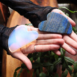 Two hands holding a heart-shaped, multicolored stone and a blue stone.