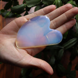 Hand holding a heart-shaped, iridescent crystal with green leaves in the background