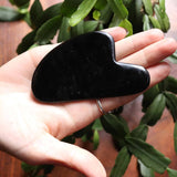 Heart-shaped black obsidian stone held in a hand with green leaves in the background