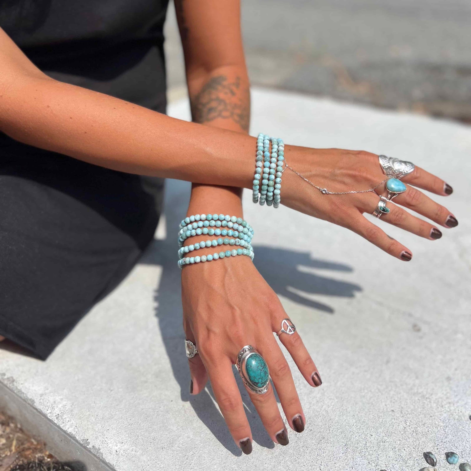 Person wearing multiple turquoise rings and larimar bracelets on a blurred outdoor background
