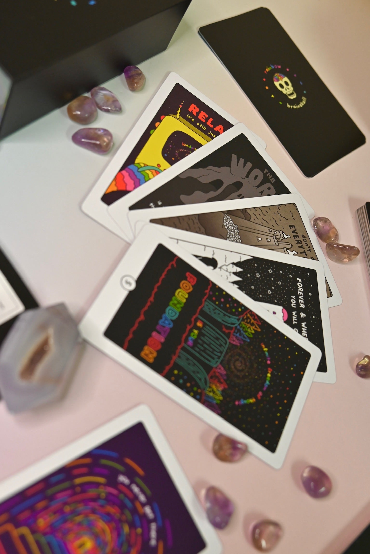 The contents of the Rainbow Brainskull Oracle Deck on a pink and blue background.