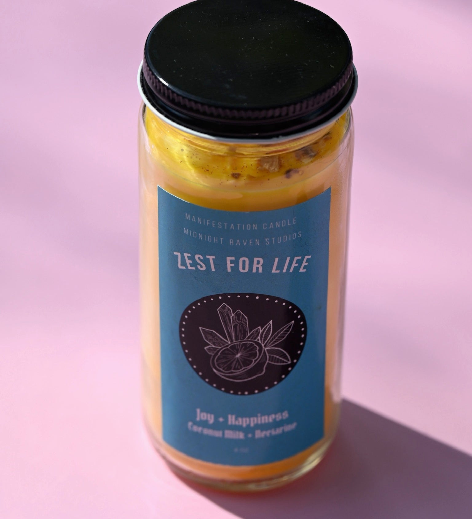 The Zest for Life Spell Candle with Herbs and Crystals on a pink background.