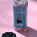 The Chill the F*ck Out Spell Candle with Herbs and Crystals on a pink background with its lid off and to the side.