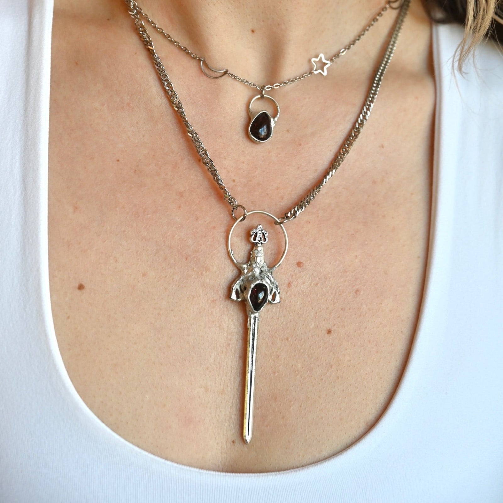 Someone wearing the Sterling Silver Garnet Sword Necklace and the Garnet Sterling Silver Celestial Necklace.