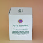 The side of the box of the Amethyst Crystal Bath Bomb on a pink background.