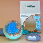 The Amazonite Crystal Bath Bomb out of the packaging surrounded by agate pieces all on a light pink background.