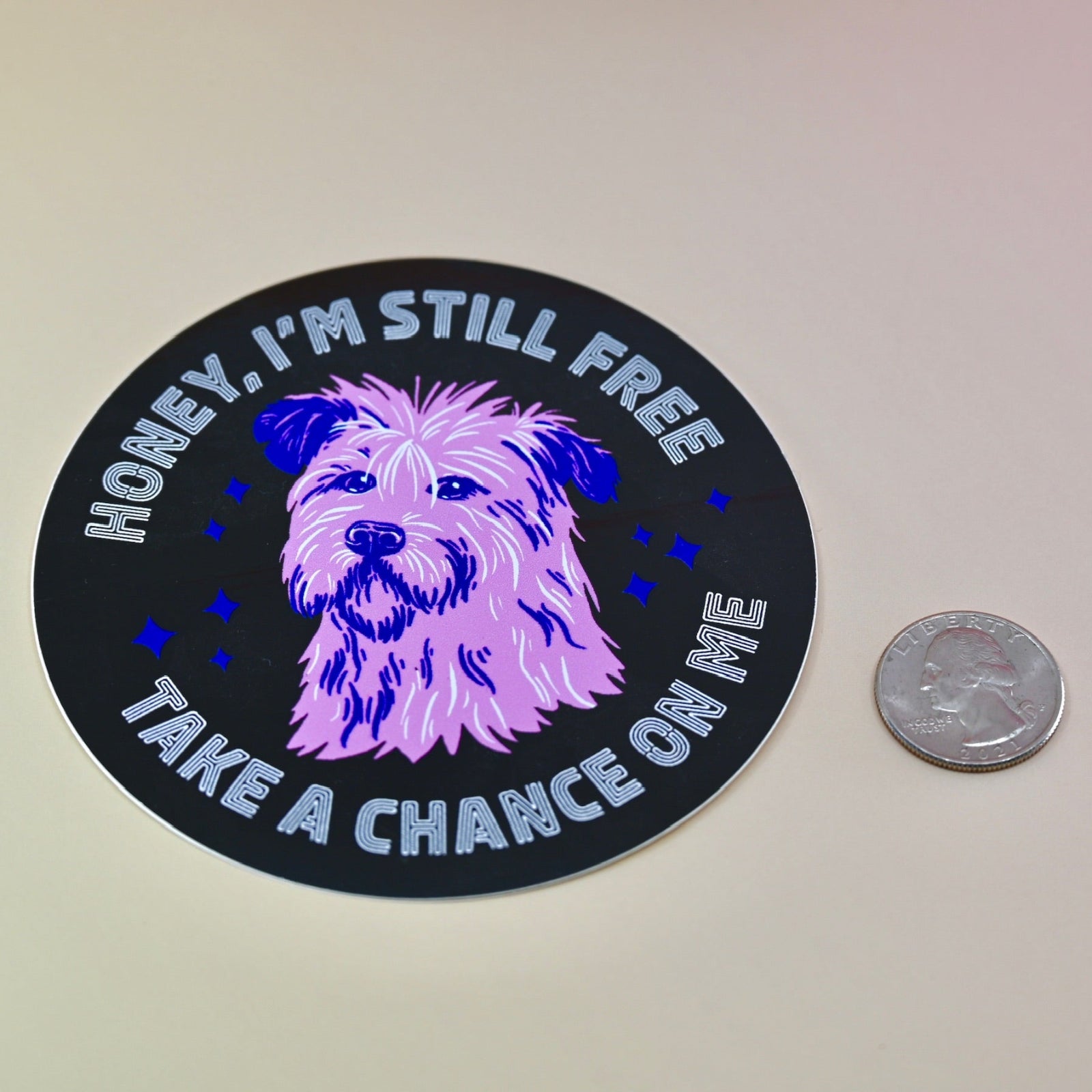 The Honey I'm Still Free Dog Sticker next to a quarter on a light peach-colored background.