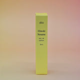 The box of the Hinoki Sesame 5ml Unisex Eau de Parfum Travel Sprayer on a pink and yellow background.