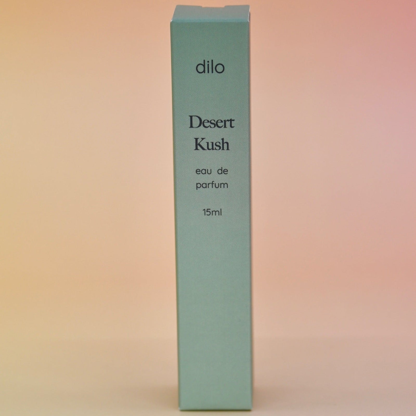 The box of the Desert Kush 15ml Unisex Eau de Parfum Travel Sprayer on alight pink background.