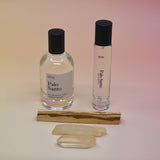 The Palo Santo 15ml Unisex Eau de Parfum Travel Sprayer and the regular size on a light pink background with a stick of palo santo in front of the bottles.