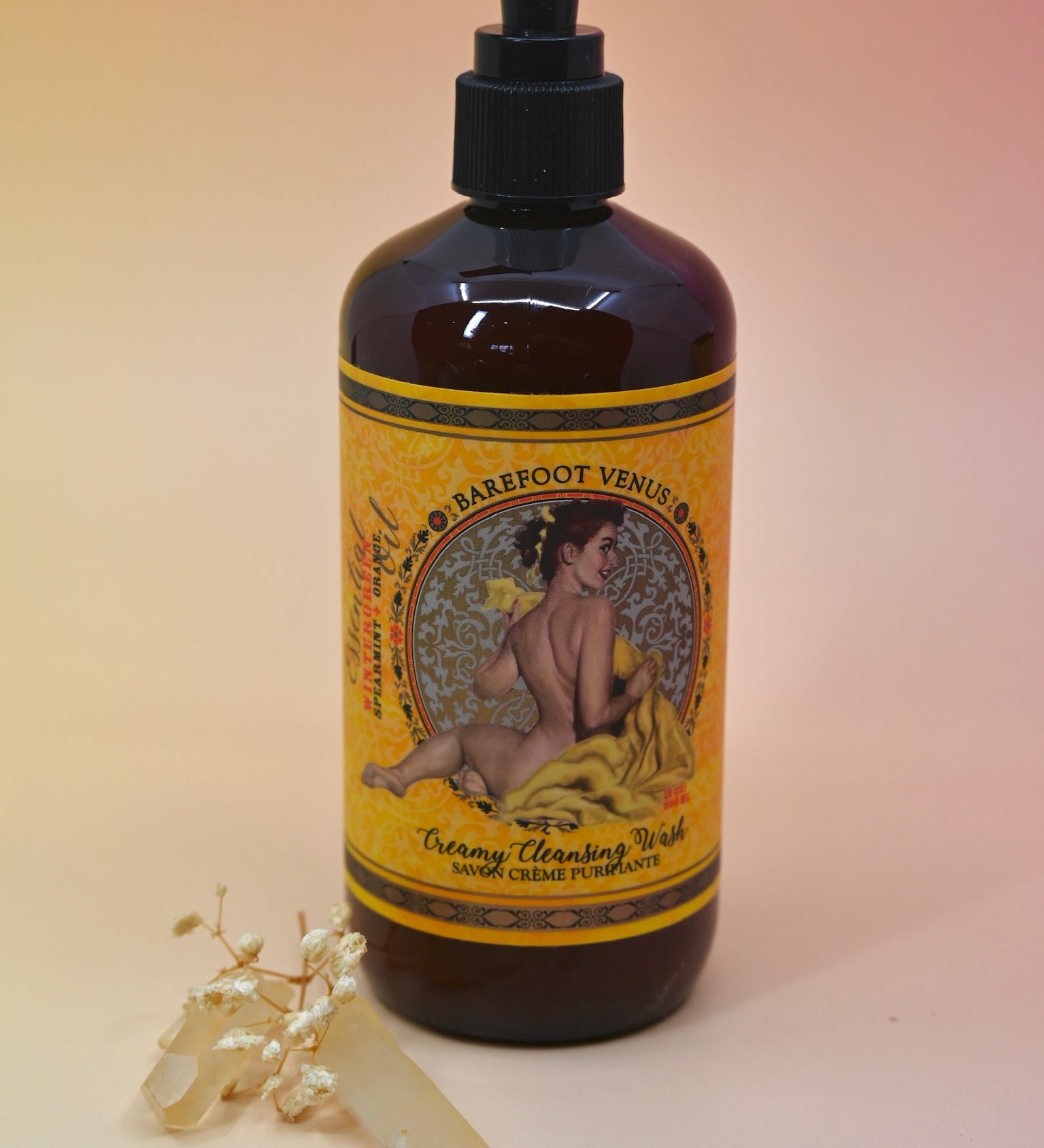 The Essential Oil Cleansing Hand & Body Wash with a crystal in front of it on a light pink background.