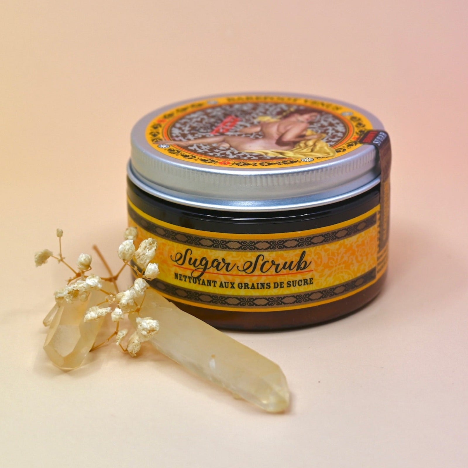 The Essential Oil Sugar Body Scrub with a crystal in front of it on a light pink background.