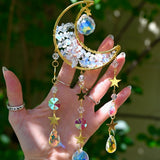 Someone holding the Opalite Crystal Moon Suncatcher with greenery in the background.