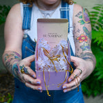 Someone holding the box of the Fairy Lights Suncatchers - Pack of 7 Suncatchers in front of a cream-colored brick wall with greenery.