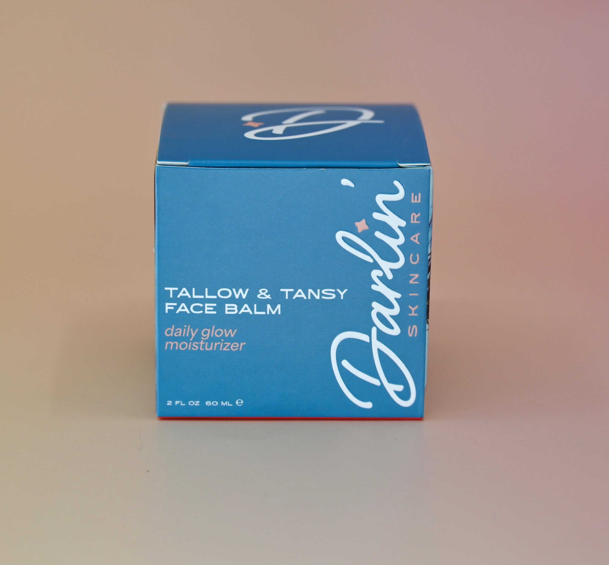 A blue jar of Darlin' Skincare Tallow & Tansy Face Balm daily glow moisturizer on a pink background.