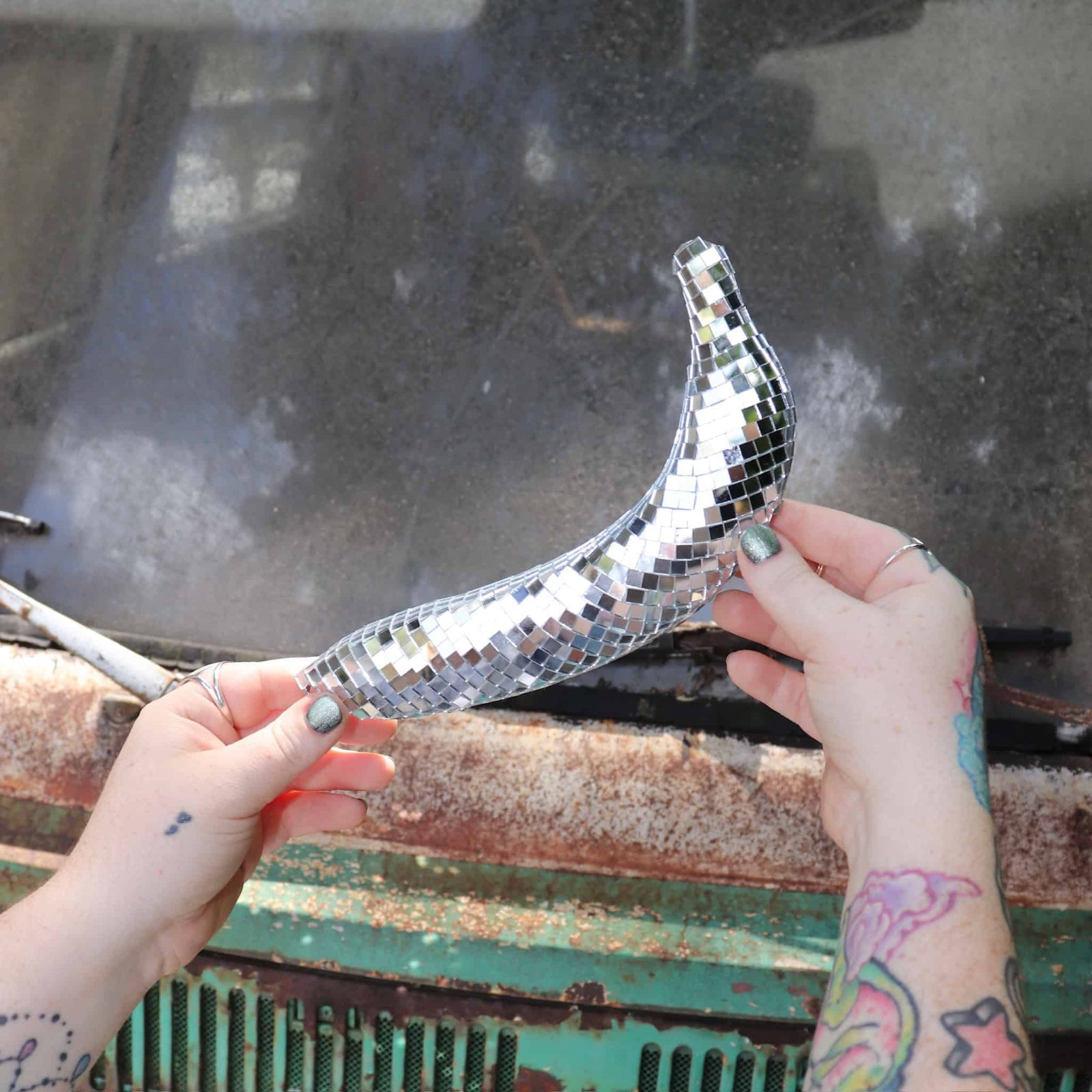 Person holding a disco ball shaped like a banana against a rusty metal surface.