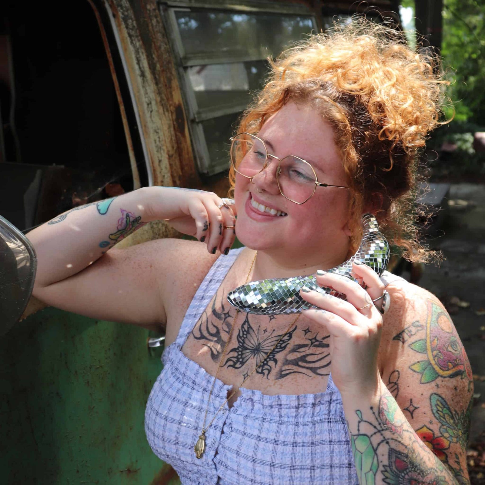 Person with tattoos holding a metallic object, standing next to a vehicle.