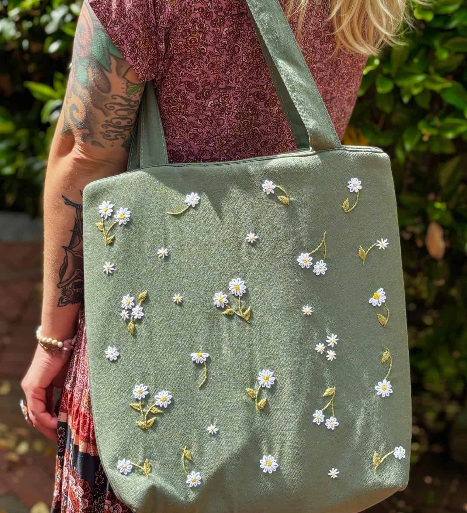 Blonde woman wearing a floral dress and carrying a sage green linen tote bag with hand-embroidered white daisies