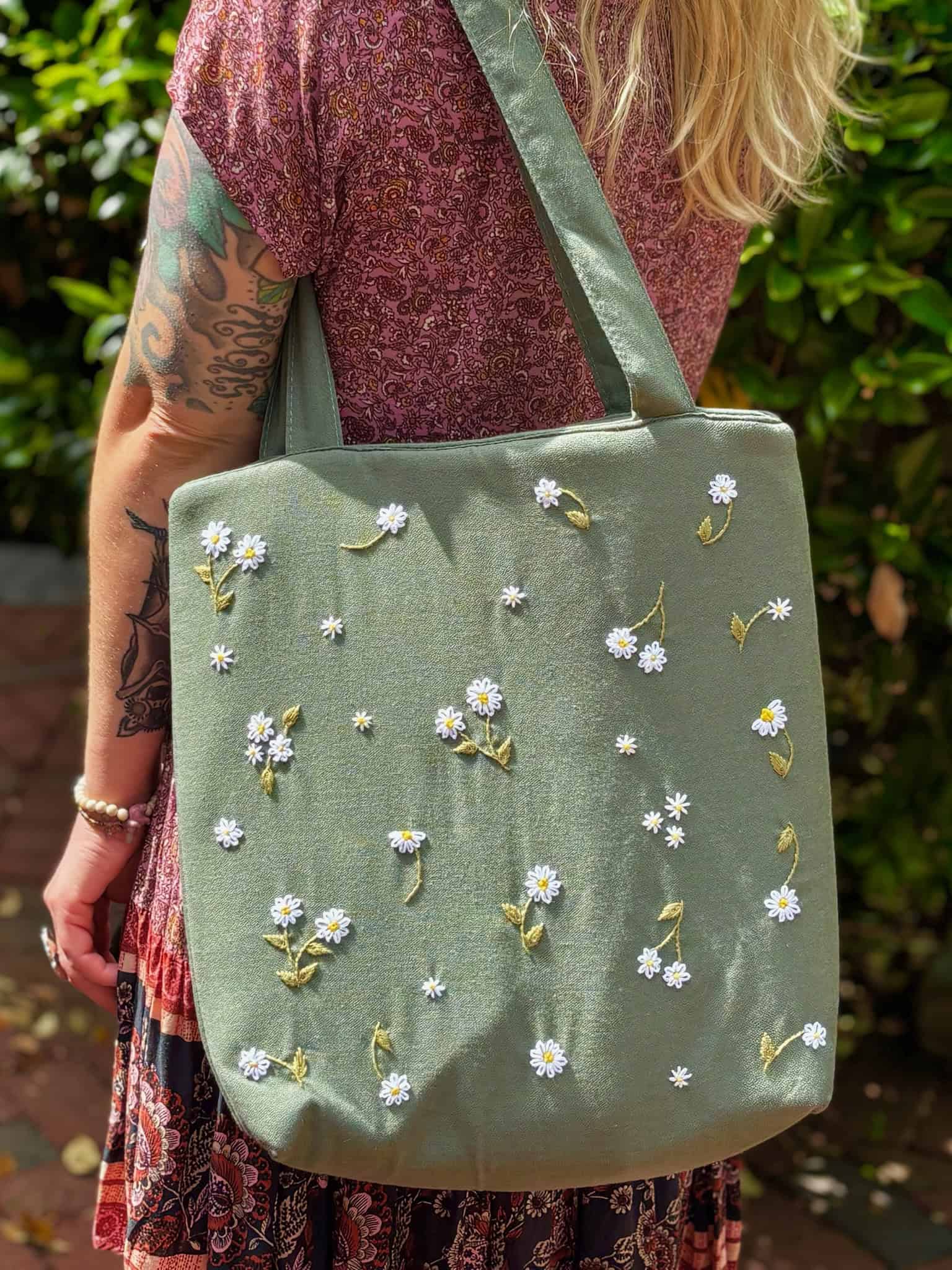 Blonde woman wearing a floral dress and carrying a sage green linen tote bag with hand-embroidered white daisies