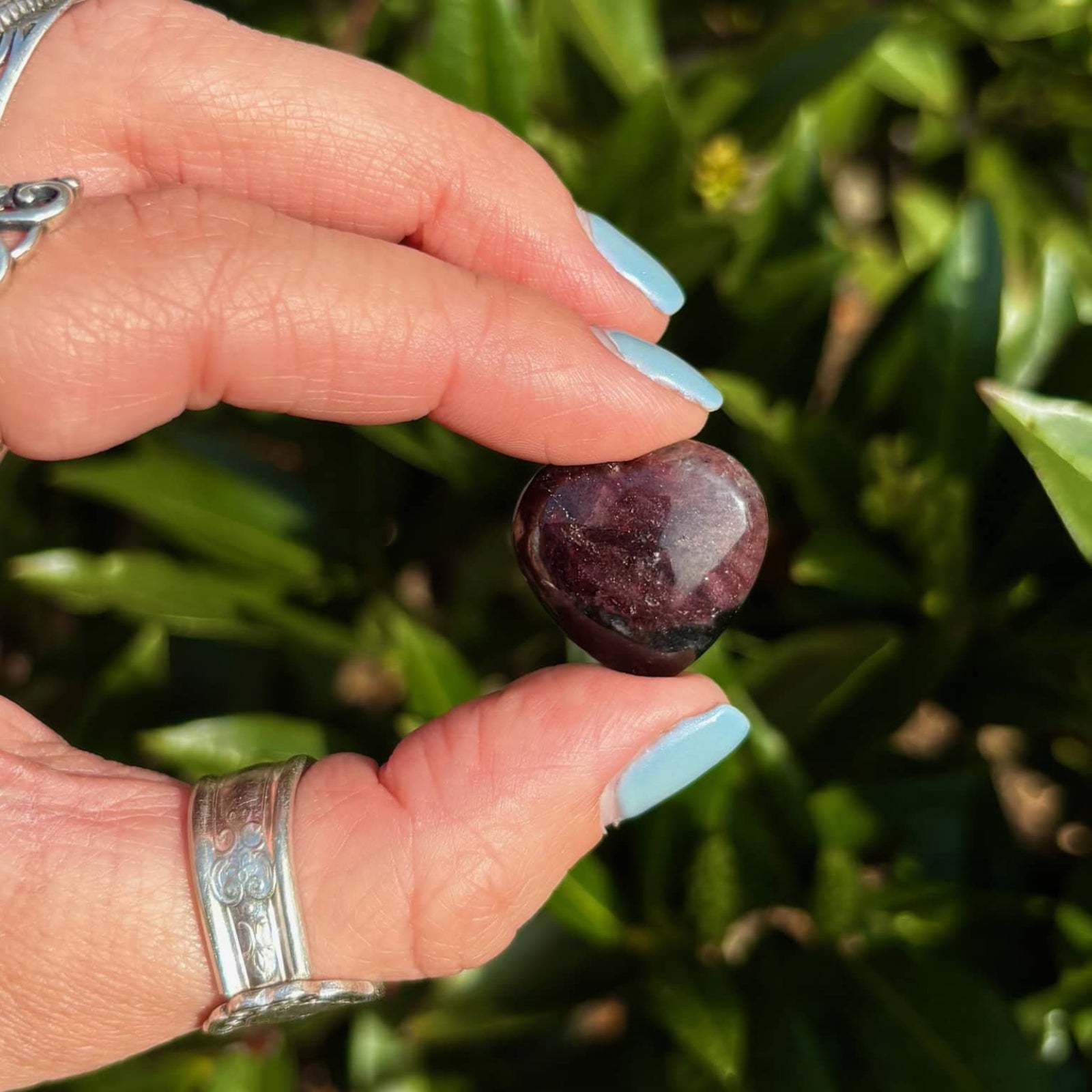 Hand holding a purple stone with green foliage in the background