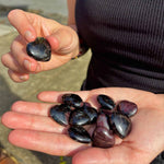 Person holding black stones in their hands by a body of water