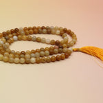 Golden Healer 108 Mala Necklace on pink and orange background