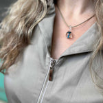Person wearing a gray jacket with a zipper, featuring a necklace with a pendant.