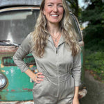 Woman in a beige jumpsuit standing in front of an old green truck with trees in the background