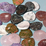A collection of heart-shaped worry stones in various colors and patterns, displayed on a blue surface.
