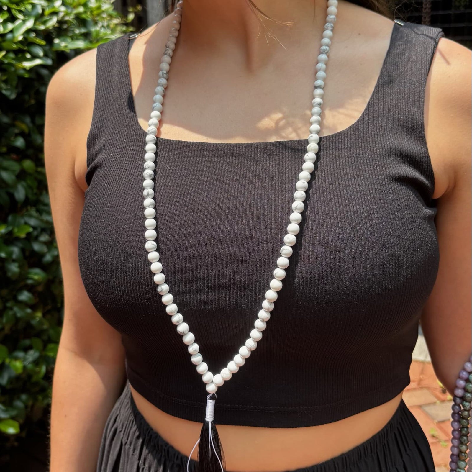 model wearing a black tank top in front of greenery with a howlite mala around her neck
