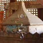 Someone holding the Prisma Hanging #36 Brass & Purple Suncatcher in front of a wooden background.