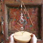 Someone holding the Prisma Tabletop #4 Diamond Tree Brass Suncatcher in front of a wooden background.